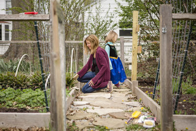 A mother works in her garden while a small child in costume stands by