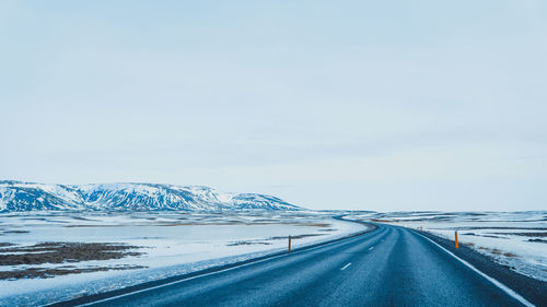 Empty road by snowcapped mountain against sky