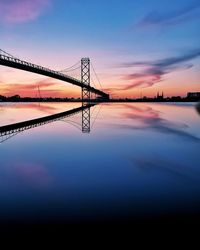 Symmetry view of silhouette bridge over river against dramatic sky during sunset