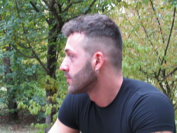 Portrait of young man looking away against trees