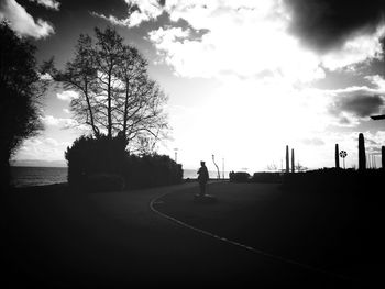 Trees on road against cloudy sky