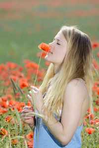 Side view of young woman smelling red poppy at field