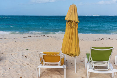 Chairs and table on beach by sea against sky