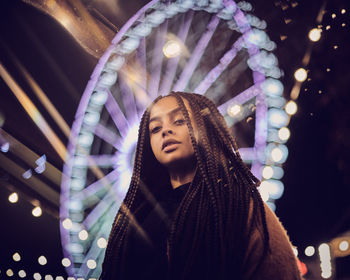 Portrait of woman standing against illuminated ferris wheel at night