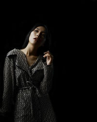 Young woman looking away while standing against black background