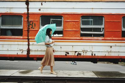 Side view of woman with umbrella walking at railroad station