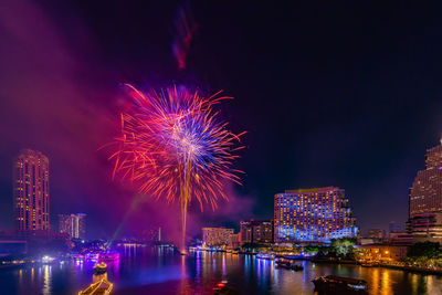 Firework display over illuminated city against sky at night