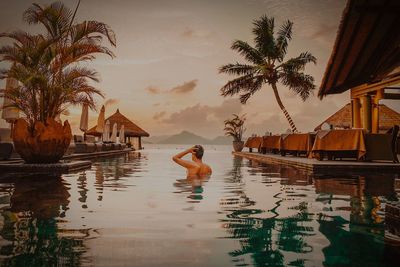 Man swimming in infinity pool against sky during sunset