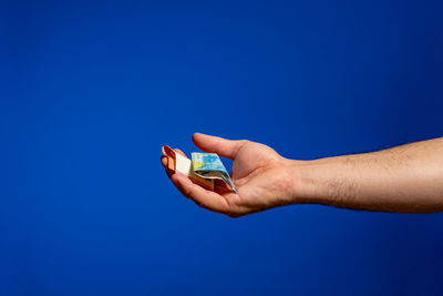 Cropped hand of man holding banknotes against blue background