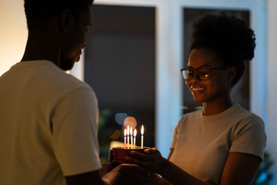 Young happy black couple holding small homemade cake while celebrating anniversary at home
