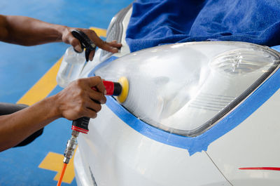 Cropped hands of man cleaning car with equipment in garage
