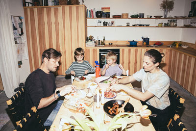 Family having dinner while sitting at dining table in kitchen