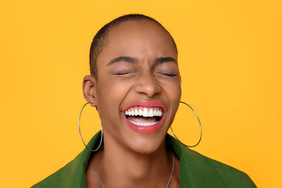 Close-up of woman with eyes closed laughing against yellow background