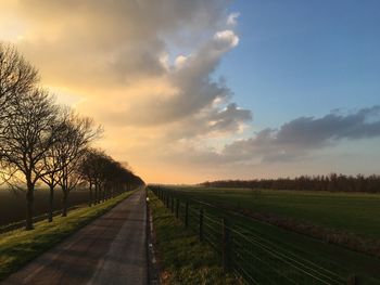 Road amidst field against sky during sunset