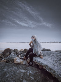 Woman sitting on rock by sea against sky