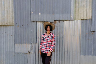 Portrait of woman in hat standing against corrugated iron