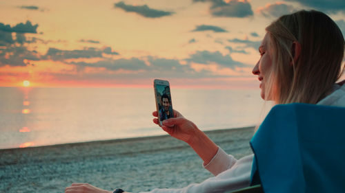Woman photographing at beach against sky
