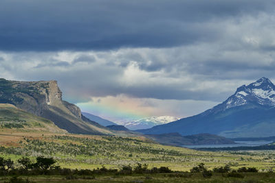Vast open landscape in patagonia with dramatic sky and rainbow over a valley, snow covered mountains