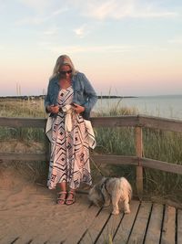 Woman standing with dog on promenade against sky during sunset