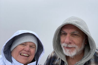 Close-up portrait of happy senior couple wearing warm clothing against clear sky