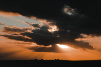 Scenic view of silhouette field against dramatic sky during sunset