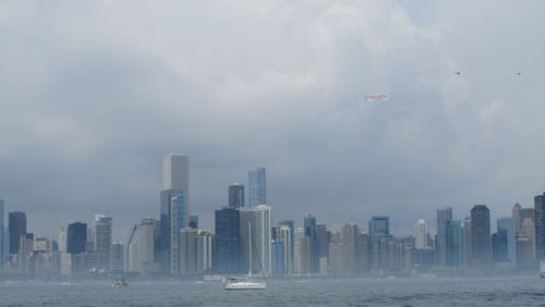 Buildings in city by sea against cloudy sky