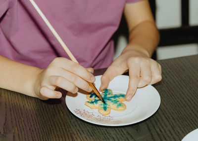 One girl is coloring cookies while sitting at the table.