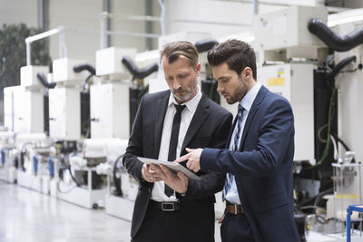 Two businessmen sharing tablet in factory shop floor