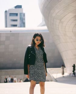 Portrait of young woman standing against building in city