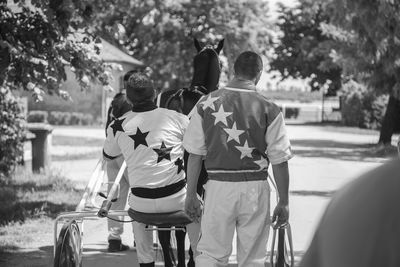 Rear view of jockeys and horse on road during sunny day