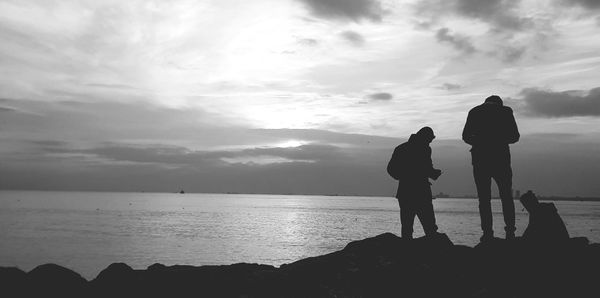 Silhouette friends at beach against cloudy sky