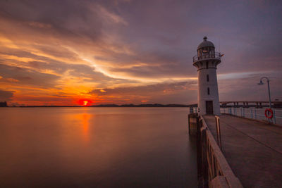 Lighthouse by sea against sky during sunset