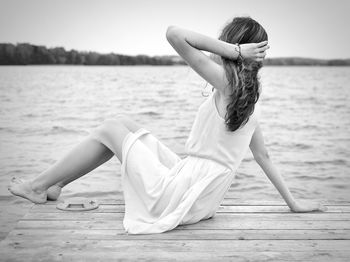 Side view of young woman sitting on pier over lake