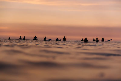 Tourists with surfboards in sea during vacations at sunset