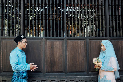 Wedding couple wearing traditional clothing while standing by wooden wall