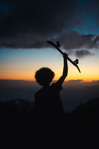 Young man holding his skate during sunset