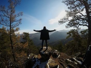 Man with arms outstretched standing against sky