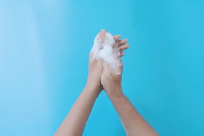 Close-up of woman hand with soap sud against blue background