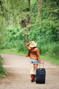 Rear view full length of woman walking with luggage on road at forest