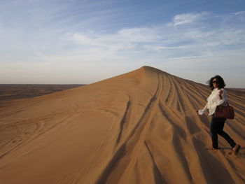 Woman walking on sand at desert against sky