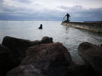 Man on rock in sea against sky