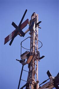 Low angle view of old railroad crossing sign against clear blue sky