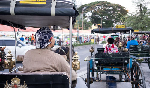 Rear view of people sitting in horse-drawn carriage on street in city