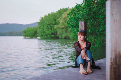 Full length portrait of man sitting on lake against trees