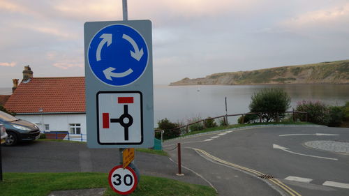 Road sign by sea against sky