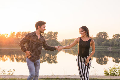 Young couple standing by lake against sky