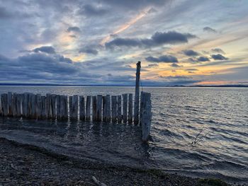 Wooden posts on beach against sky during sunset