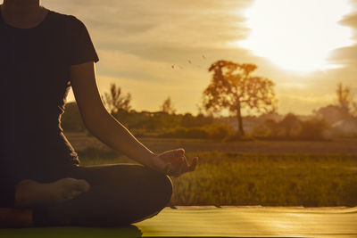 Midsection of woman sitting at park during sunset