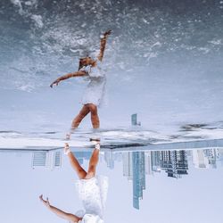 Low section of woman dancing while reflecting on puddle in city