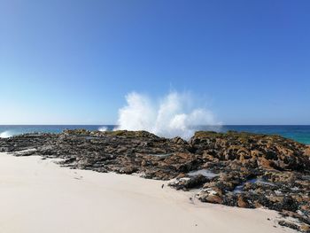 Panoramic view of waves on beach against clear blue sky